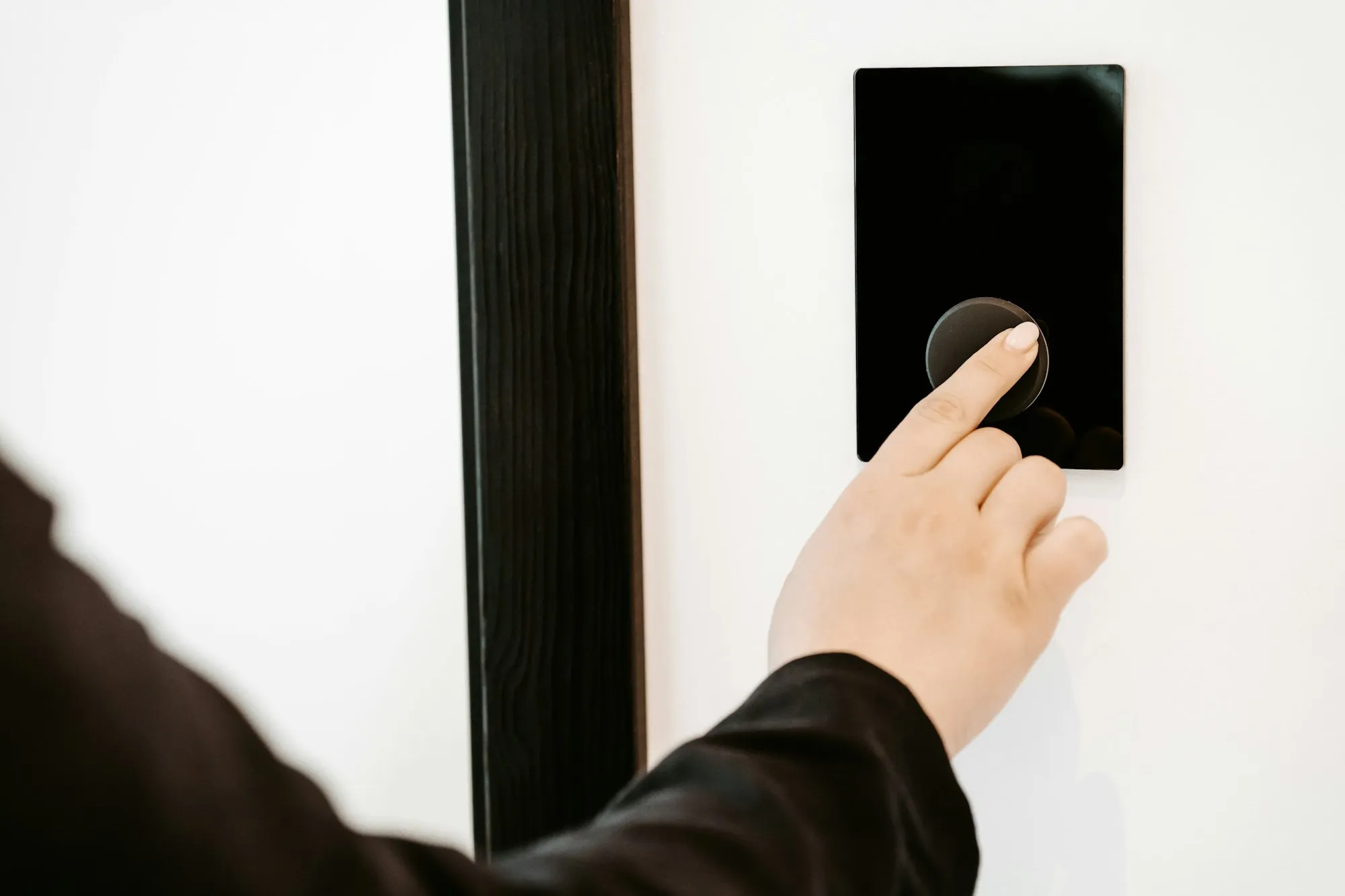Hand pressing a wall-mounted access reader beside a door